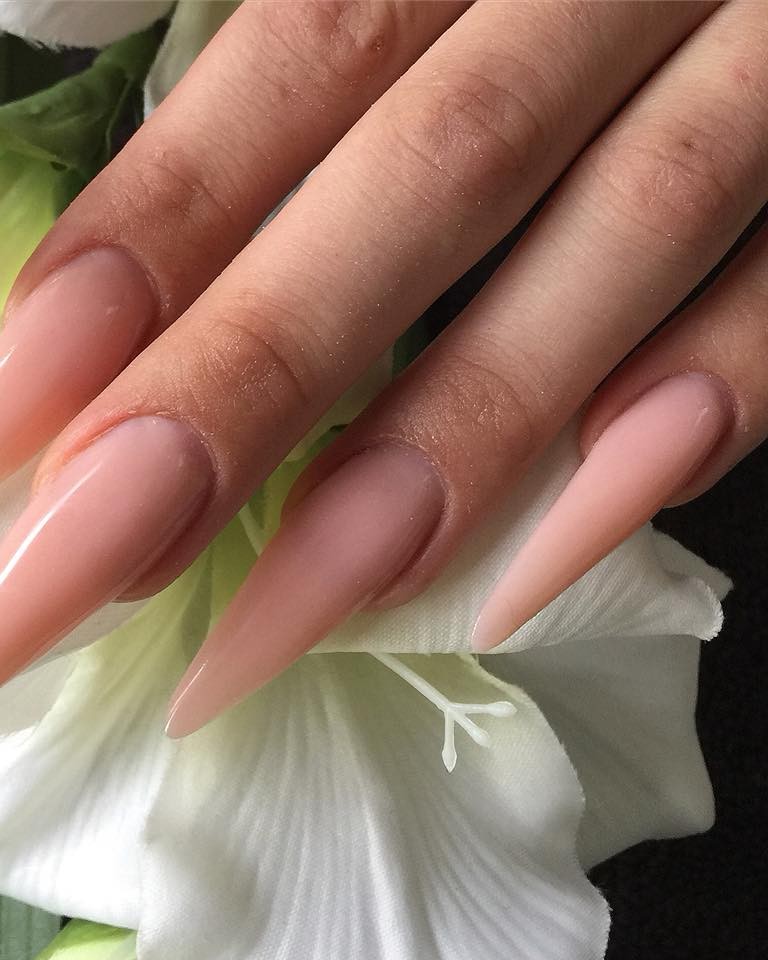 Lange naturelkleurige stilettonagels op een witte bloem